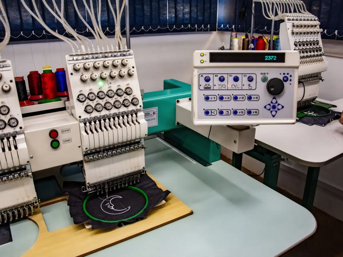 Bordadeira industrial de várias cabeças com cones de linha coloridos numa oficina de bordado